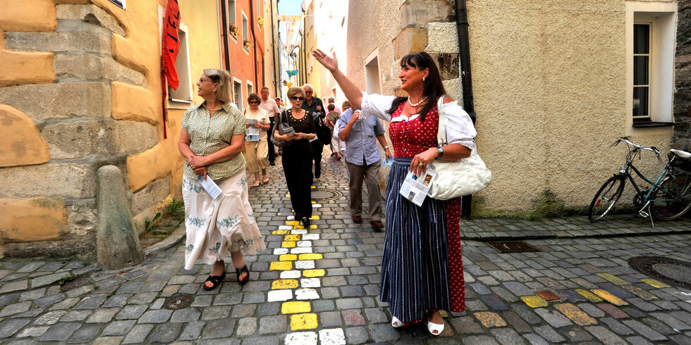 Eine Gruppe von Menschen spaziert durch die bunte Kopfsteinpflasterstraße in Passaus Altstadt.